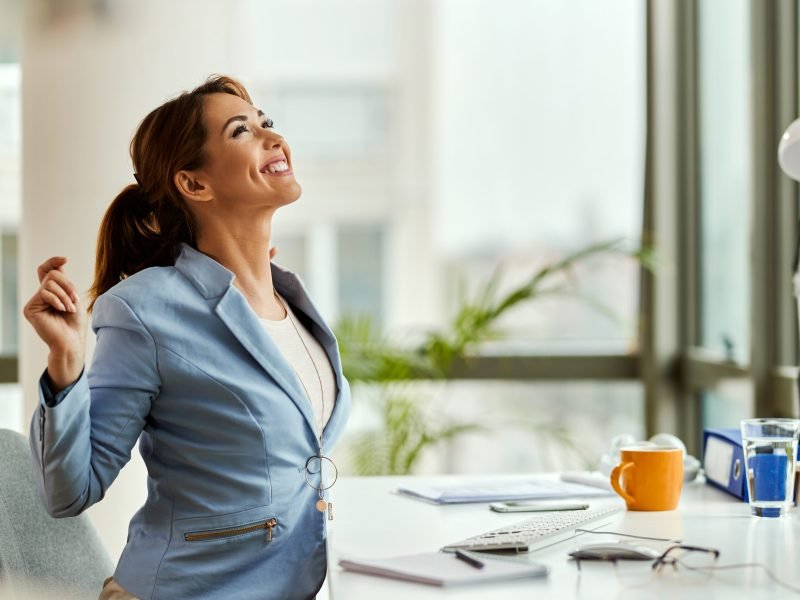 Happy female entrepreneur looking up while stretching in the office.